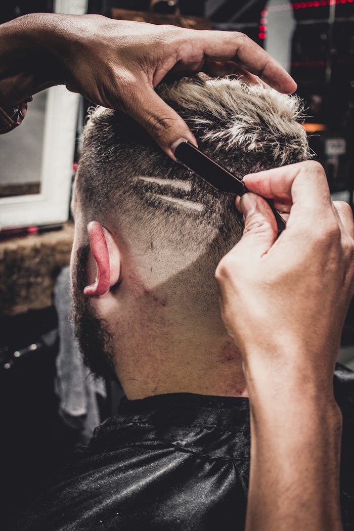 Services A man receives a detailed haircut with a straight razor at a barbershop, showcasing modern style.